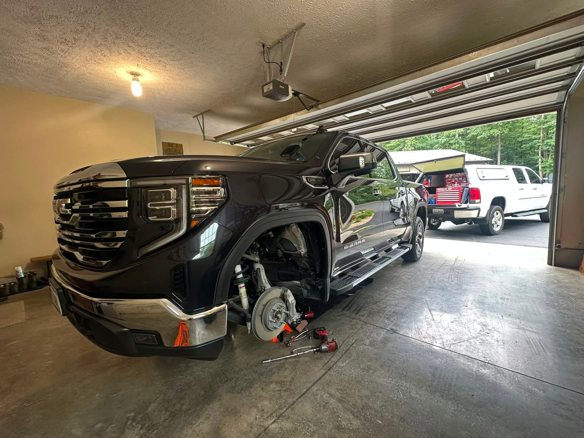 GMC Sierra on jack stands with the front wheel off for brake work in a home garage