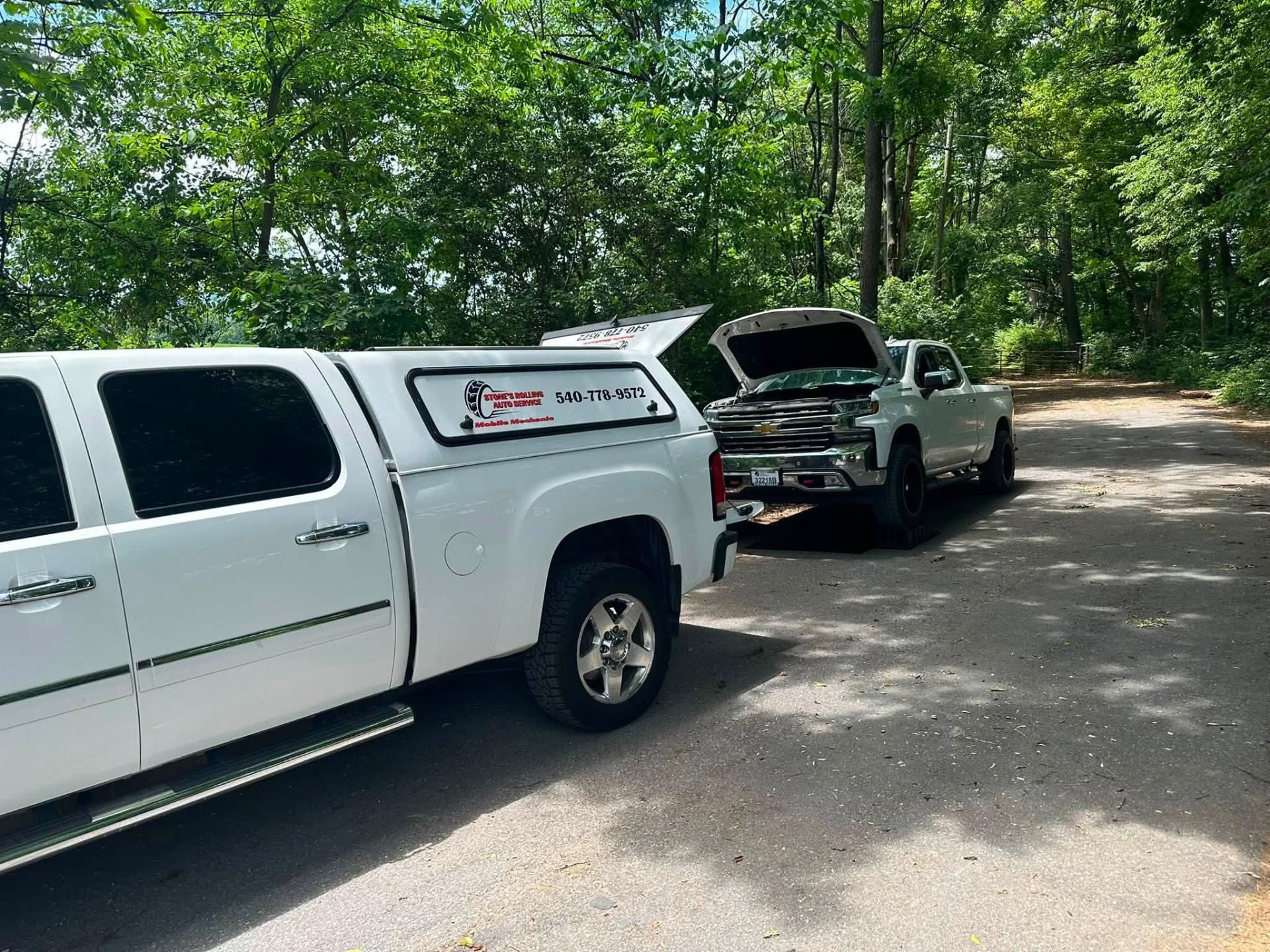 Stone's Rolling Auto Service truck parked beside a pickup with its hood up on a wooded road